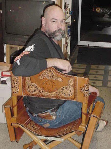 WC sitting in a custom leather directors chair he made that has leather script bags and he has a leather quick sheath on his hip.